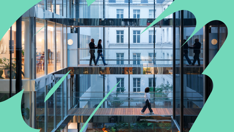 Two team members have a conversation while walking across a walkway in the company’s multi-floor office while another employee walks across a walkway beneath them